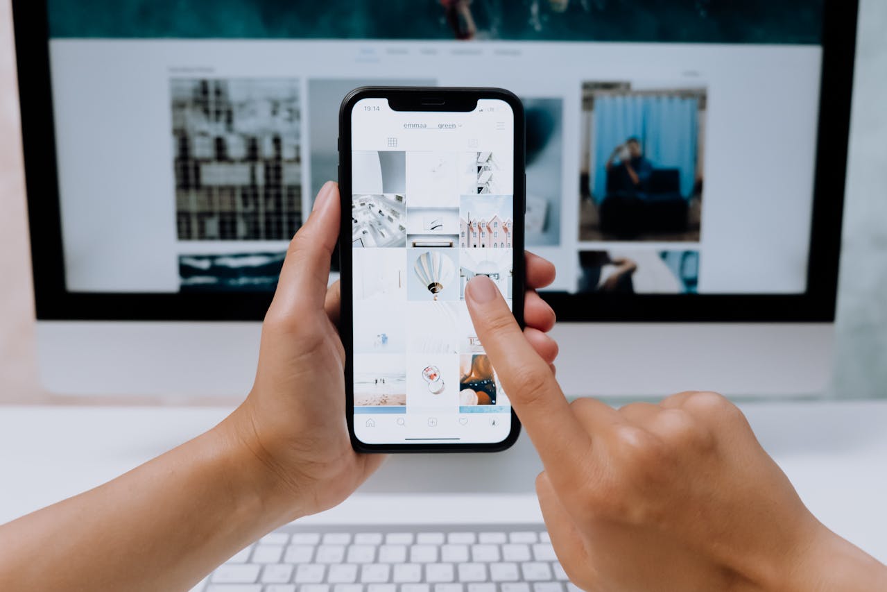 Hands holding a mobile phone reviewing a website while a desktop displays the same site — checking how a website performs across devices